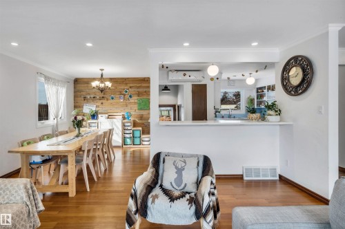 The property features hardwood flooring throughout, a dining area with a wooden accent wall, and a pass-through opening to the kitchen - 4208 89 Street Nw, Edmonton, AB - Indoor