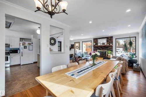 Open concept living area with hardwood flooring, a dining area featuring a light wood table, and a living room with a brick fireplace - 4208 89 Street Nw, Edmonton, AB - Indoor Photo Showing Dining Room