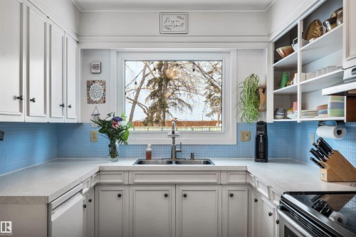 The kitchen features white cabinetry, light countertops, a blue tiled backsplash, and a window above the sink - 4208 89 Street Nw, Edmonton, AB - Indoor Photo Showing Kitchen With Double Sink