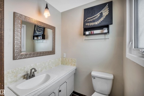 The bathroom features a vanity with an integrated sink and a textured backsplash, complemented by a large framed mirror and a pendant light fixture - 4208 89 Street Nw, Edmonton, AB - Indoor Photo Showing Bathroom