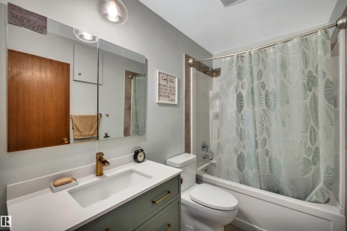 The bathroom features a vanity with a white countertop and a rectangular sink, a gold-toned faucet, and cabinetry with gold-toned handles - 4208 89 Street Nw, Edmonton, AB - Indoor Photo Showing Bathroom