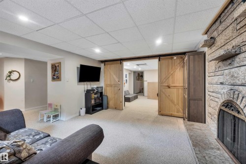 Living area featuring a textured stone fireplace with hearth, recessed lighting, and barn-style sliding doors - 4208 89 Street Nw, Edmonton, AB - Indoor Photo Showing Basement With Fireplace