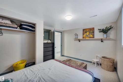 The property features a room with carpeted flooring, a built-in closet, and a light-colored accent wall with a mounted shelf - 4208 89 Street Nw, Edmonton, AB - Indoor Photo Showing Bedroom