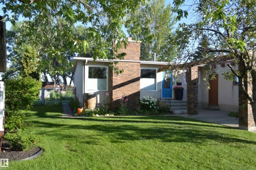 The property features a brick chimney, a vibrant blue entry door, and a well-maintained lawn with mature trees and garden beds - 4208 89 Street Nw, Edmonton, AB - Outdoor