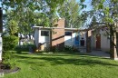 The property features a brick chimney, a vibrant blue entry door, and a well-maintained lawn with mature trees and garden beds - 4208 89 Street Nw, Edmonton, AB  - Outdoor 