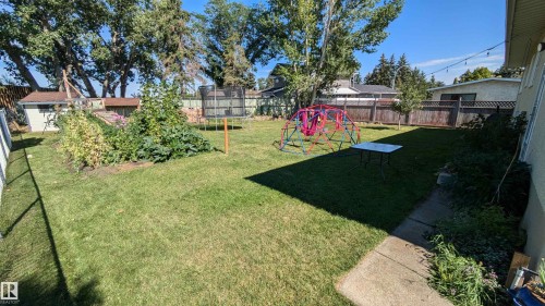 The property features an extensive green lawn, a garden bed, a storage shed, and a wooden fence - 4208 89 Street Nw, Edmonton, AB - Outdoor With Backyard