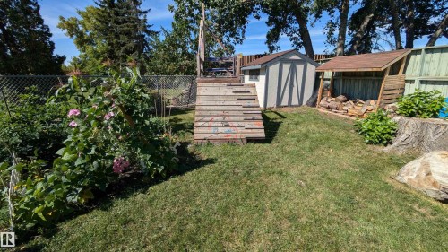 The property features a spacious yard with a lawn, mature trees, and a garden area with flowering plants - 4208 89 Street Nw, Edmonton, AB - Outdoor
