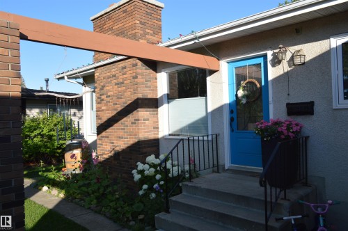 The property features a brick chimney, a concrete porch with steps, and a blue front door with a window - 4208 89 Street Nw, Edmonton, AB - Outdoor