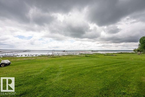 Expansive green lawn extending to the water's edge, featuring multiple docks and a tranquil body of water - 90 2001 Twp Rd, Rural Leduc County, AB 