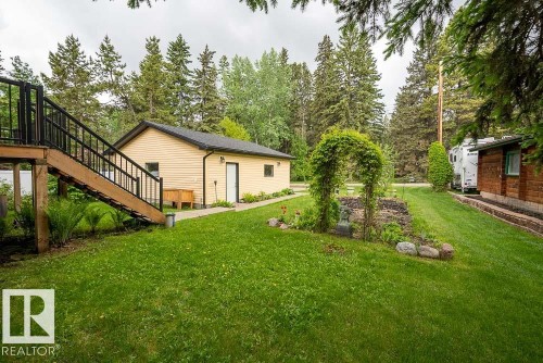 Spacious backyard featuring a manicured lawn, an elevated wood deck with black railings, and a detached structure with light-toned siding - 90 2001 Twp Rd, Rural Leduc County, AB 