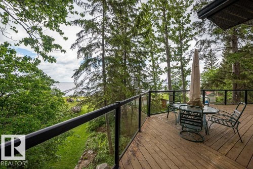 Exterior wood deck featuring a clear panel railing system with black handrails and a tree-lined perimeter - 90 2001 Twp Rd, Rural Leduc County, AB 