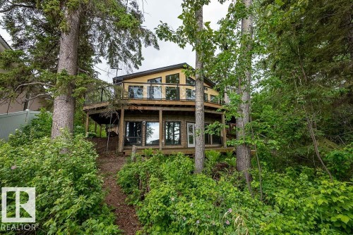 Multi-level residence featuring a wrap-around deck with glass railings and wood flooring - 90 2001 Twp Rd, Rural Leduc County, AB 