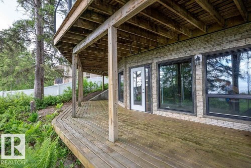 Spacious wooden deck with support beams, stone veneer siding, large windows with dark trim, and a white glass-paneled door - 90 2001 Twp Rd, Rural Leduc County, AB 
