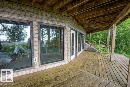 Spacious wood deck featuring an exposed timber ceiling, direct exterior access, and a stone facade - 90 2001 Twp Rd, Rural Leduc County, AB 