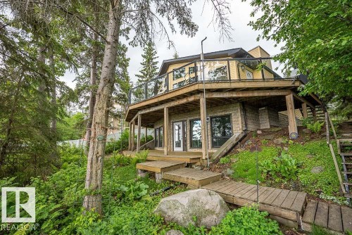 Multi-level hillside residence featuring a prominent upper deck with glass railings and a lower-level covered patio - 90 2001 Twp Rd, Rural Leduc County, AB 
