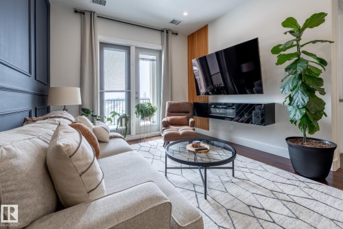 The living area features wood flooring, a textured area rug, and a door leading to an outdoor space - 454 6079 Maynard Way, Edmonton, AB - Indoor Photo Showing Living Room