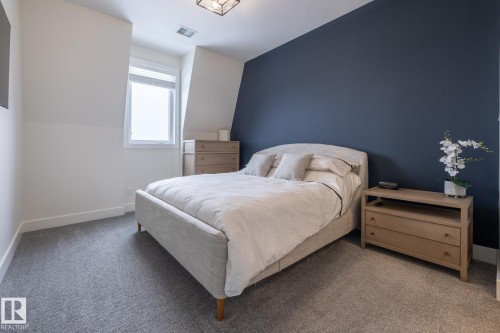 This bedroom features light gray carpeting, a window, and a dark accent wall - 454 6079 Maynard Way, Edmonton, AB - Indoor Photo Showing Bedroom