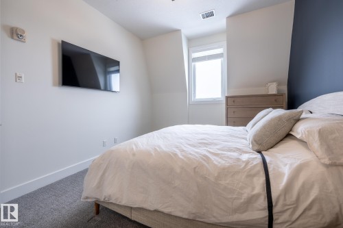 This sleeping area features sloped ceilings, a window, and a wall-mounted television - 454 6079 Maynard Way, Edmonton, AB - Indoor Photo Showing Bedroom