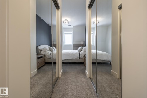 Hallway from ensuite to primary bedroom features mirrored closet doors and carpeted flooring - 454 6079 Maynard Way, Edmonton, AB - Indoor Photo Showing Bedroom