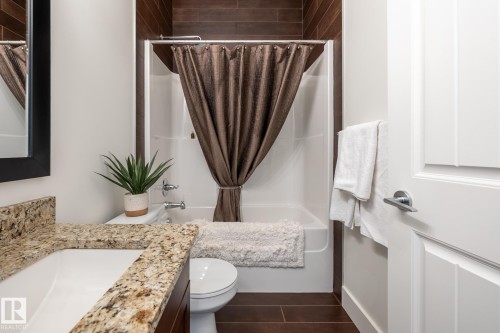Bathroom featuring a granite countertop vanity with a white sink, a bathtub with a shower, and dark wood-look floor tiling - 454 6079 Maynard Way, Edmonton, AB - Indoor Photo Showing Bathroom