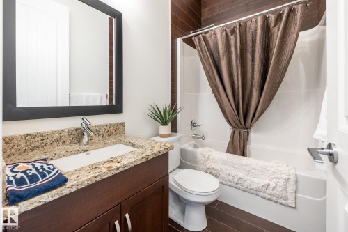 Bathroom featuring a vanity with a granite countertop and an integrated sink, a mirror with a dark frame, and a shower-tub combination with a shower curtain - 454 6079 Maynard Way, Edmonton, AB - Indoor Photo Showing Bathroom