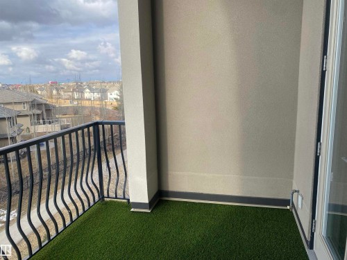 The property features a balcony with artificial turf flooring, a black metal railing, and views of the surrounding neighborhood - 454 6079 Maynard Way, Edmonton, AB - Outdoor With Exterior