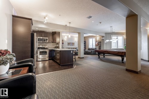 Spacious entertainment area featuring a kitchen with stainless steel appliances, a billiards table, and large windows providing natural light - 454 6079 Maynard Way, Edmonton, AB - Indoor Photo Showing Kitchen