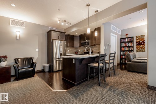 The property features a kitchen with dark cabinetry, stainless steel appliances, and a central island with bar seating - 454 6079 Maynard Way, Edmonton, AB - Indoor Photo Showing Kitchen With Upgraded Kitchen