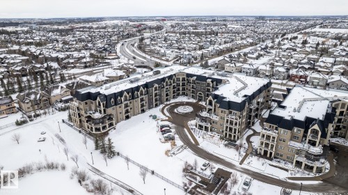 A modern building with a distinctive dark roof, showcasing several balconies and a central driveway entrance - 454 6079 Maynard Way, Edmonton, AB - Outdoor With View