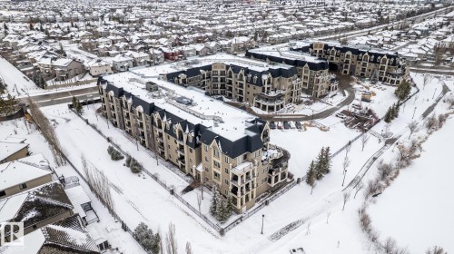 This property features a multi-story building with a distinctive dark roof and light-colored facade, surrounded by a snow-covered landscape - 454 6079 Maynard Way, Edmonton, AB - Outdoor