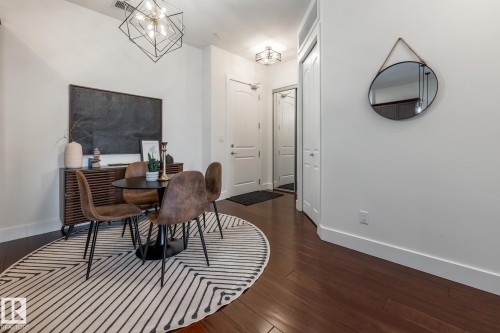 This inviting dining area features dark hardwood flooring, a modern chandelier, and a decorative mirror - 454 6079 Maynard Way, Edmonton, AB - Indoor