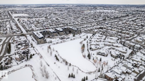 Aerial view of the community, showcasing residential properties and a central pond, all covered in snow - 454 6079 Maynard Way, Edmonton, AB - Outdoor With View