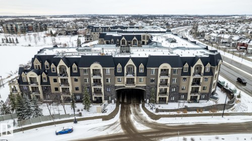 The property features a multi-story building with a distinctive facade combining stone and stucco, topped with dark sloped roofs and dormer windows - 454 6079 Maynard Way, Edmonton, AB - Outdoor With Facade