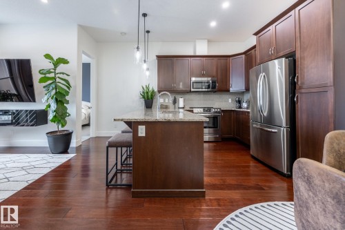Kitchen featuring rich wood cabinetry, stainless steel appliances, a granite countertop island, and pendant lighting - 454 6079 Maynard Way, Edmonton, AB - Indoor Photo Showing Kitchen