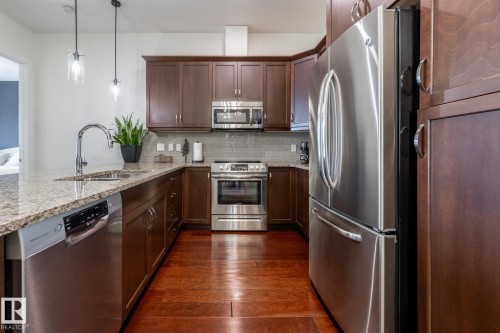The kitchen features hardwood floors, granite countertops, stainless steel appliances, and dark wood cabinetry - 454 6079 Maynard Way, Edmonton, AB - Indoor Photo Showing Kitchen With Double Sink With Upgraded Kitchen