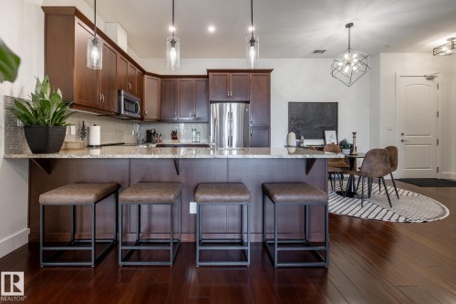 The kitchen features wood cabinetry, stainless steel appliances, and a granite countertop breakfast bar with pendant lighting - 454 6079 Maynard Way, Edmonton, AB - Indoor Photo Showing Kitchen With Upgraded Kitchen