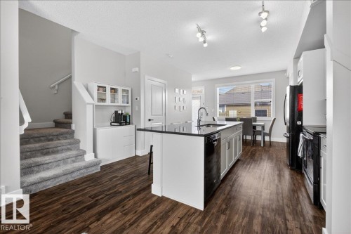 Open concept kitchen featuring dark wood flooring, a central island with a sink and dark countertop, white and grey cabinetry, and track lighting - 9034 Rosenthal Link Link, Edmonton, AB - Indoor Photo Showing Kitchen