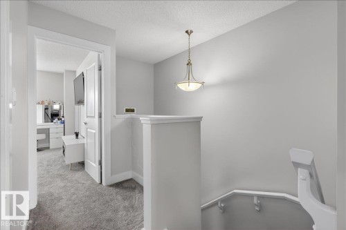 This hallway features light gray walls, plush gray carpeting, and a traditional ceiling light fixture - 9034 Rosenthal Link Link, Edmonton, AB - Indoor