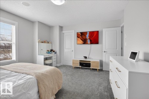 The property features a bedroom with a large window, light gray walls, and gray carpeting - 9034 Rosenthal Link Link, Edmonton, AB - Indoor Photo Showing Bedroom