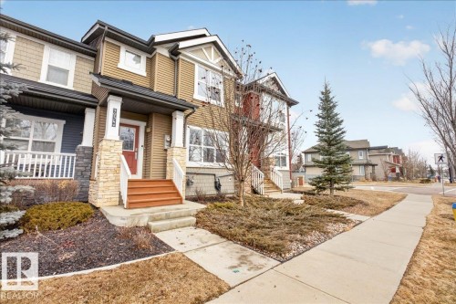 The property features an inviting entrance with a red front door, a covered porch supported by stone pillars, and a concrete pathway leading to the front steps - 9034 Rosenthal Link Link, Edmonton, AB - Outdoor With Facade