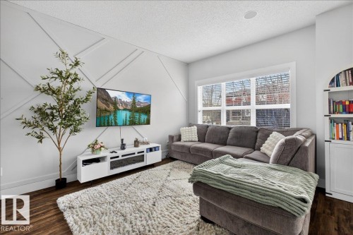 Living area featuring a detailed accent wall, hardwood flooring, and a large window with horizontal blinds - 9034 Rosenthal Link Link, Edmonton, AB - Indoor Photo Showing Living Room