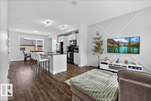 The open concept living area features hardwood style flooring, a kitchen island with seating, and a decorative accent wall - 9034 Rosenthal Link Link, Edmonton, AB - Indoor