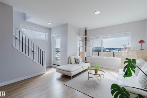 The property features light-colored flooring, a staircase with a white railing and black balusters, and large windows that provide natural light and views of the exterior - 1129 Keswick Drive, Edmonton, AB - Indoor Photo Showing Living Room