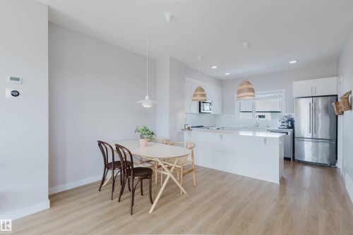 The property features an open-concept living area with light wood-style flooring, a dining area, and a kitchen with white cabinetry, stainless steel appliances, and a white subway tile backsplash - 1129 Keswick Drive, Edmonton, AB - Indoor