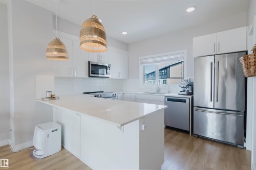 Contemporary kitchen featuring a large island with white countertops, white cabinetry, and stainless steel appliances including a refrigerator, microwave, and dishwasher - 1129 Keswick Drive, Edmonton, AB - Indoor Photo Showing Kitchen With Stainless Steel Kitchen With Upgraded Kitchen