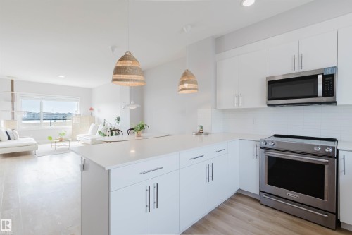The kitchen features white cabinetry, stainless steel appliances, a white subway tile backsplash, and light countertops - 1129 Keswick Drive, Edmonton, AB - Indoor Photo Showing Kitchen