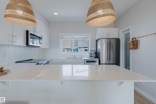 The kitchen features a spacious island with a light-colored countertop, white cabinetry with silver hardware, stainless steel appliances, and a tiled backsplash - 1129 Keswick Drive, Edmonton, AB - Indoor Photo Showing Kitchen With Stainless Steel Kitchen With Upgraded Kitchen