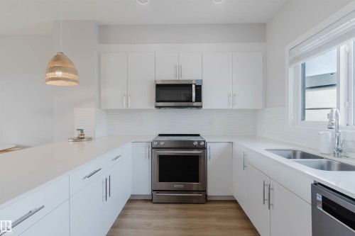 Bright kitchen featuring white cabinetry, stainless steel appliances including a microwave and range, and a double basin sink - 1129 Keswick Drive, Edmonton, AB - Indoor Photo Showing Kitchen With Double Sink With Upgraded Kitchen