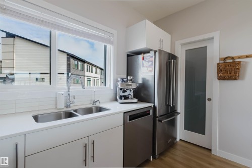 The kitchen features white cabinetry, a double basin stainless steel sink with a gooseneck faucet, a stainless steel refrigerator, and a dishwasher - 1129 Keswick Drive, Edmonton, AB - Indoor Photo Showing Kitchen With Double Sink