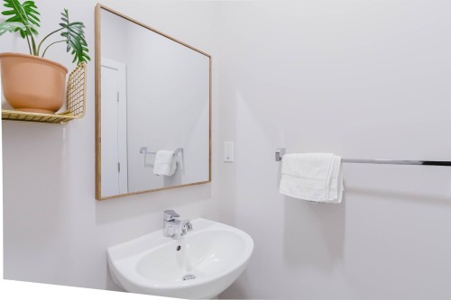 Bathroom featuring a wall-mounted sink with a chrome faucet, a rectangular mirror with a wood frame, and a chrome towel bar - 1129 Keswick Drive, Edmonton, AB - Indoor Photo Showing Bathroom